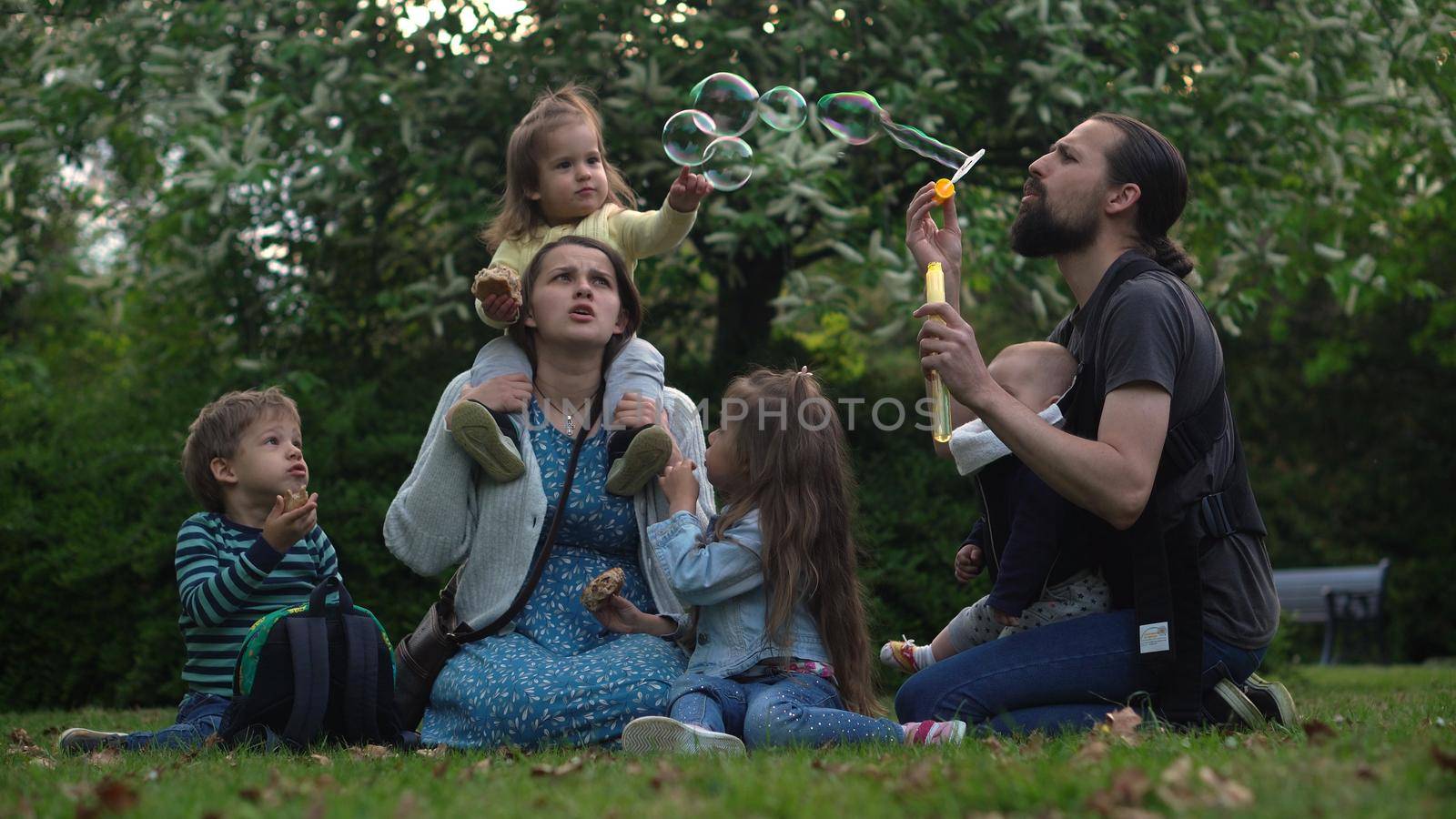 Happy family mother Father Three four Baby little siblings kids have fun blowing bubbles enjoying summer holidays in garden park. Smiling parents children spending leisure time together evening sunset.