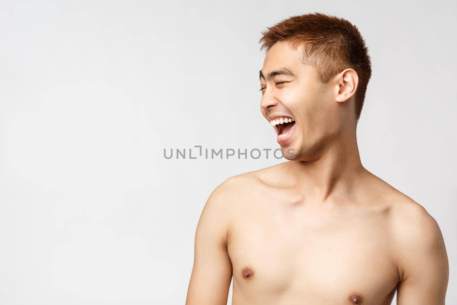 Beauty, people and home concept. Close-up portrait of handsome young asian man with naked torso, looking left and laughing out loud, having fun watching hilarious performance, white background.