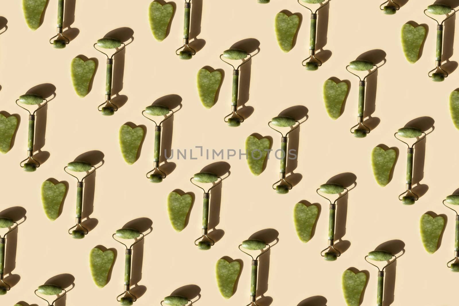 Repeating pattern with jade Gua sha scraper and facial massager on beige background. Hard light, shadows, the concept self-care. Facial care. Zero waste. Lifting and toning treatment at home.