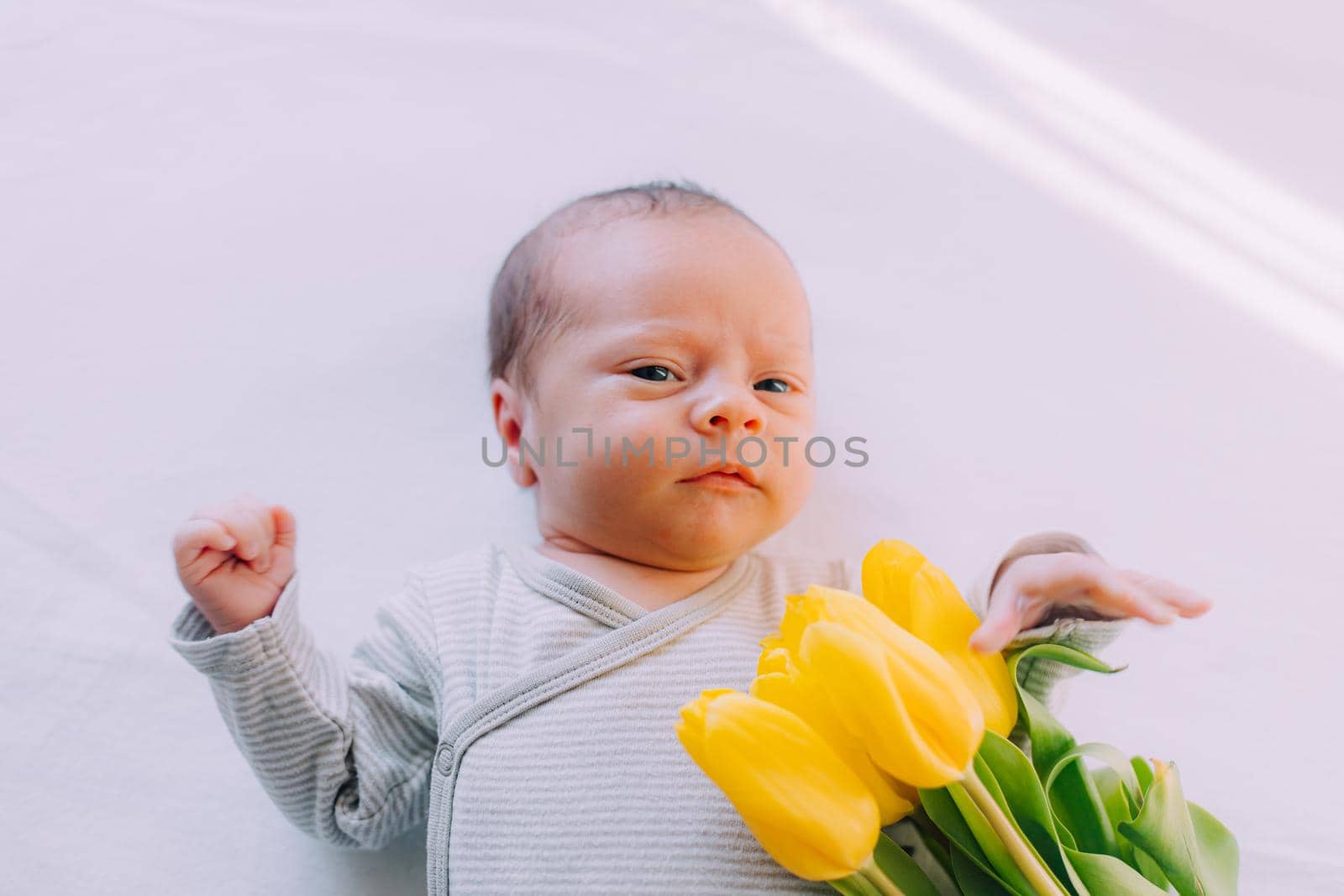 A newborn baby with a bouquet of tulips . A greeting card. March 8th. Baby and flowers. Yellow tulips