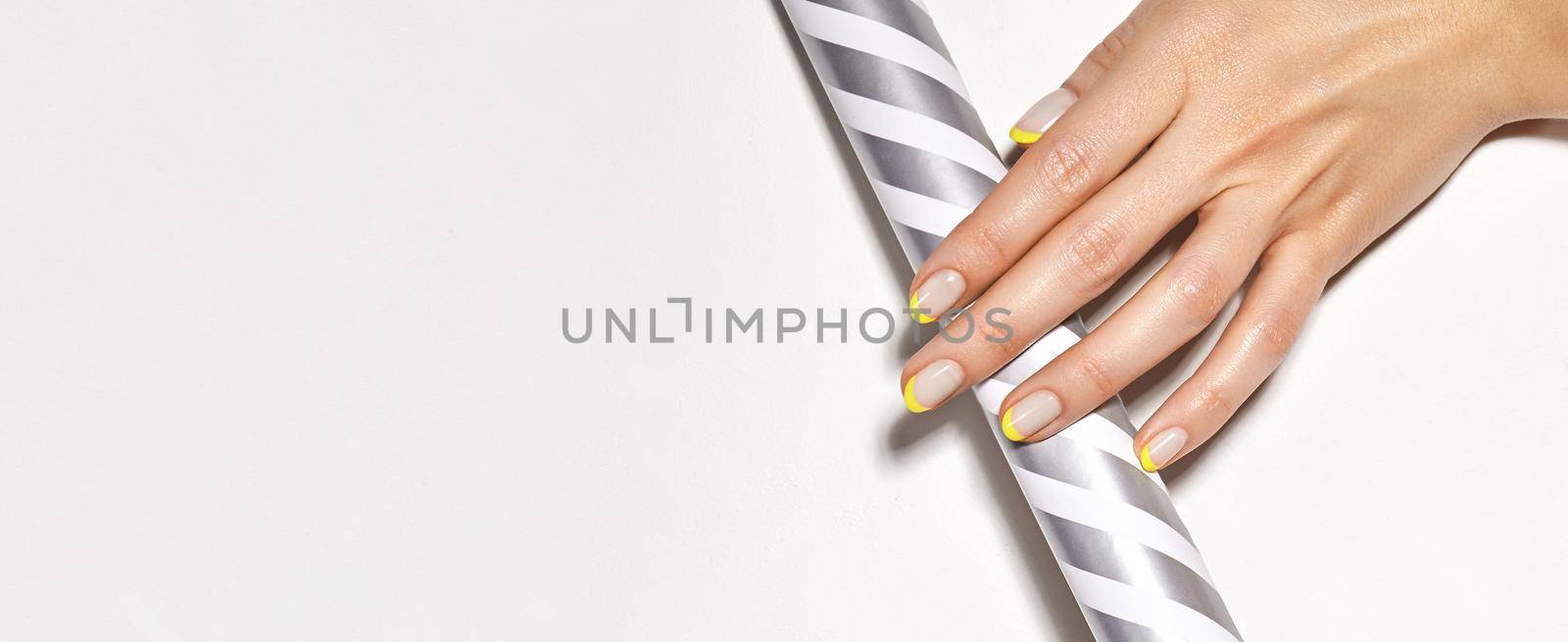 Hands with bright yellow french manicure. Nails art design. Close-up of hands with trendy neon nails on striped print by MarinaFrost