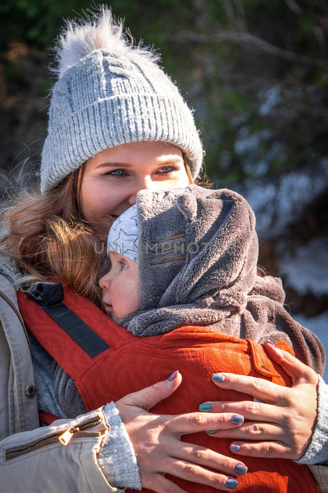 Portrait of beautiful caucasian babywearing mother with her son in baby carrier winter outdoor.
