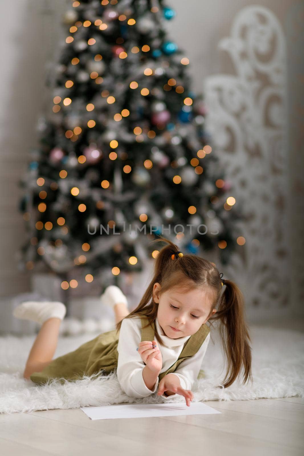 Little girl is writing a letter to santa claus against the background of Christmas trees. Vertical, copy space.