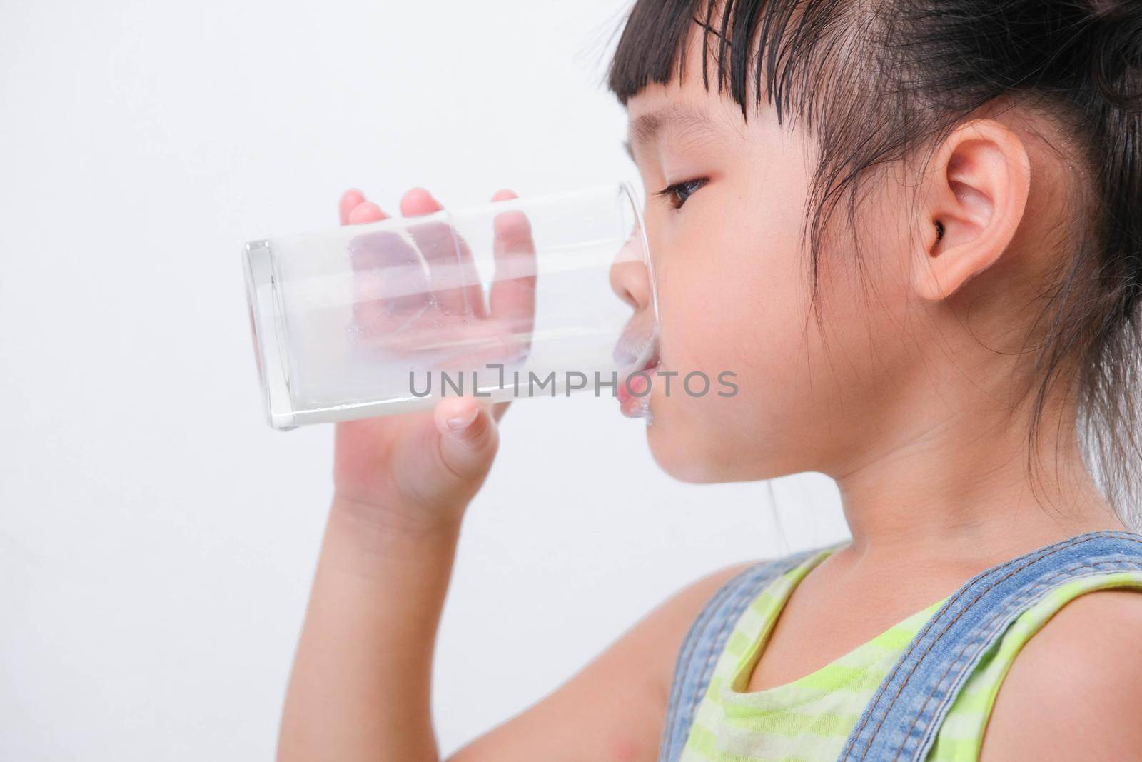 Cute little girl drinking milk from a glass isolated on white background. Little girls enjoy drinking milk before going to school. by TEERASAK