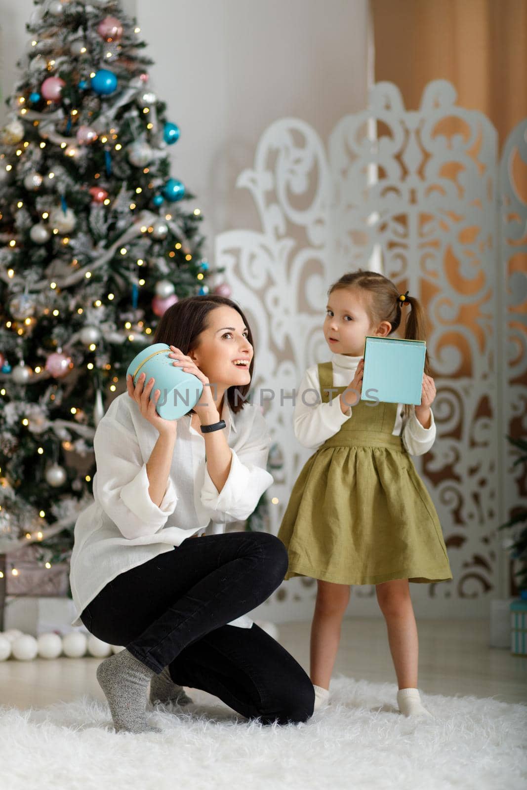 Cute little girl with her mother give each other new year gifts in christmas interior. Vertical, copy space.