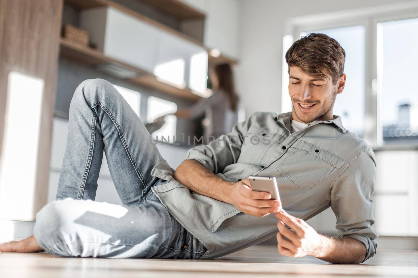 young man with smartphone sitting on kitchen floor by asdf