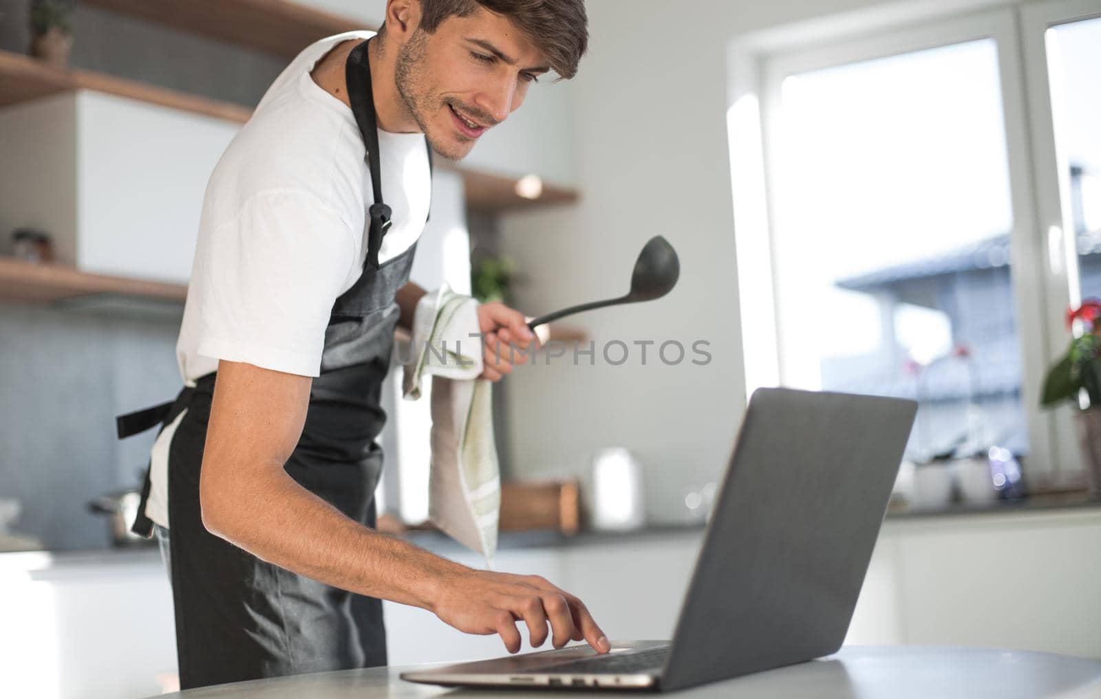 attractive young man looking at laptop screen while cooking dinner