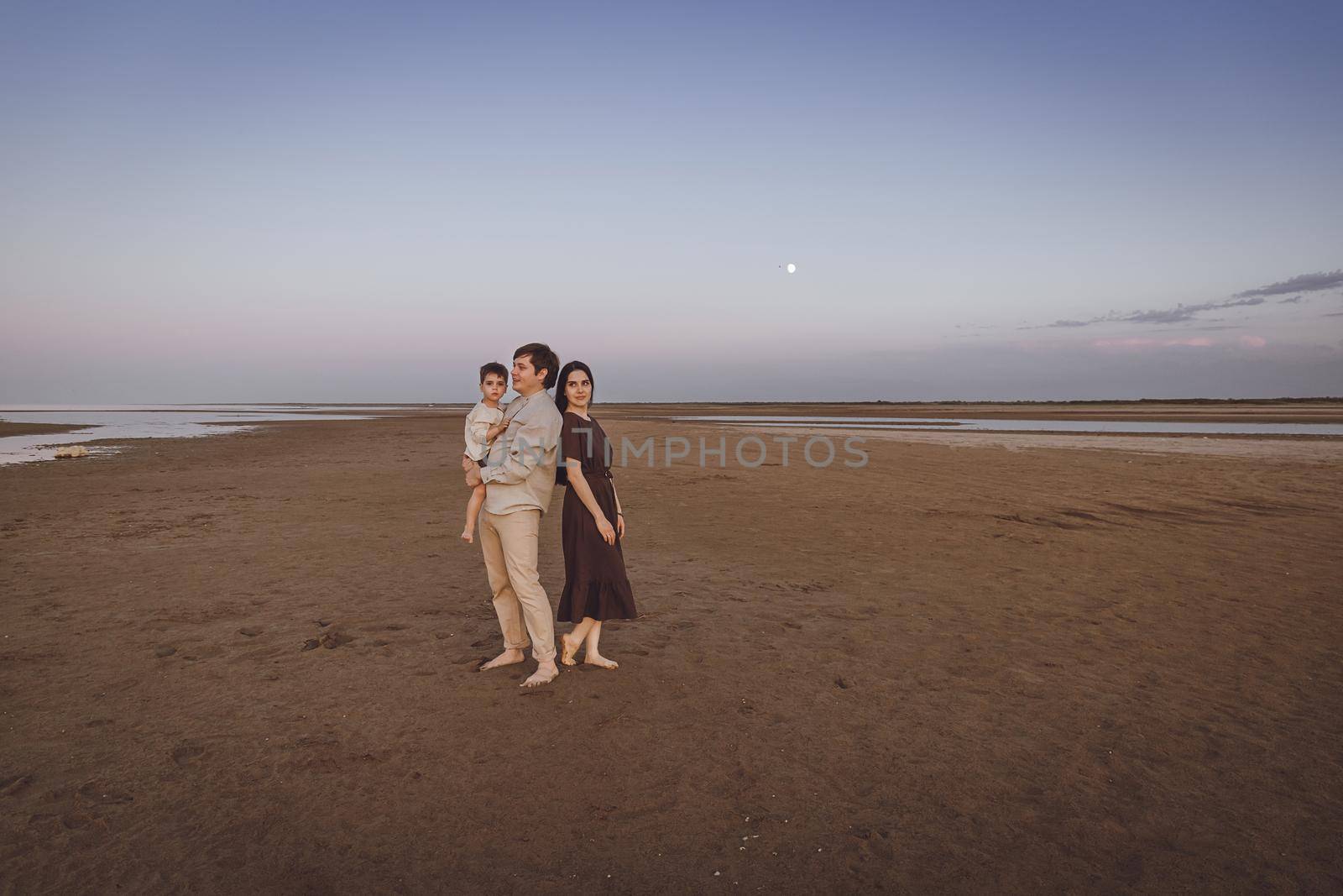 Beautiful young family on the evening beach. Family look of natural linen clothing. Copy space by Rom4ek