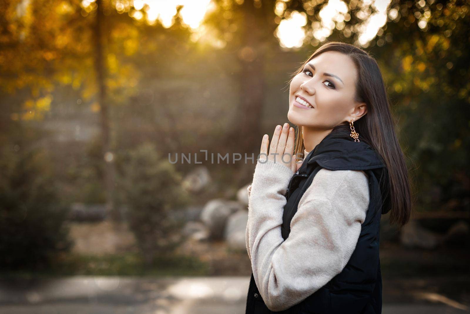 Smiling young woman on the right side of the photo stands outdoors in autumn in a warm sweater and sleeveless jacket. High quality photo