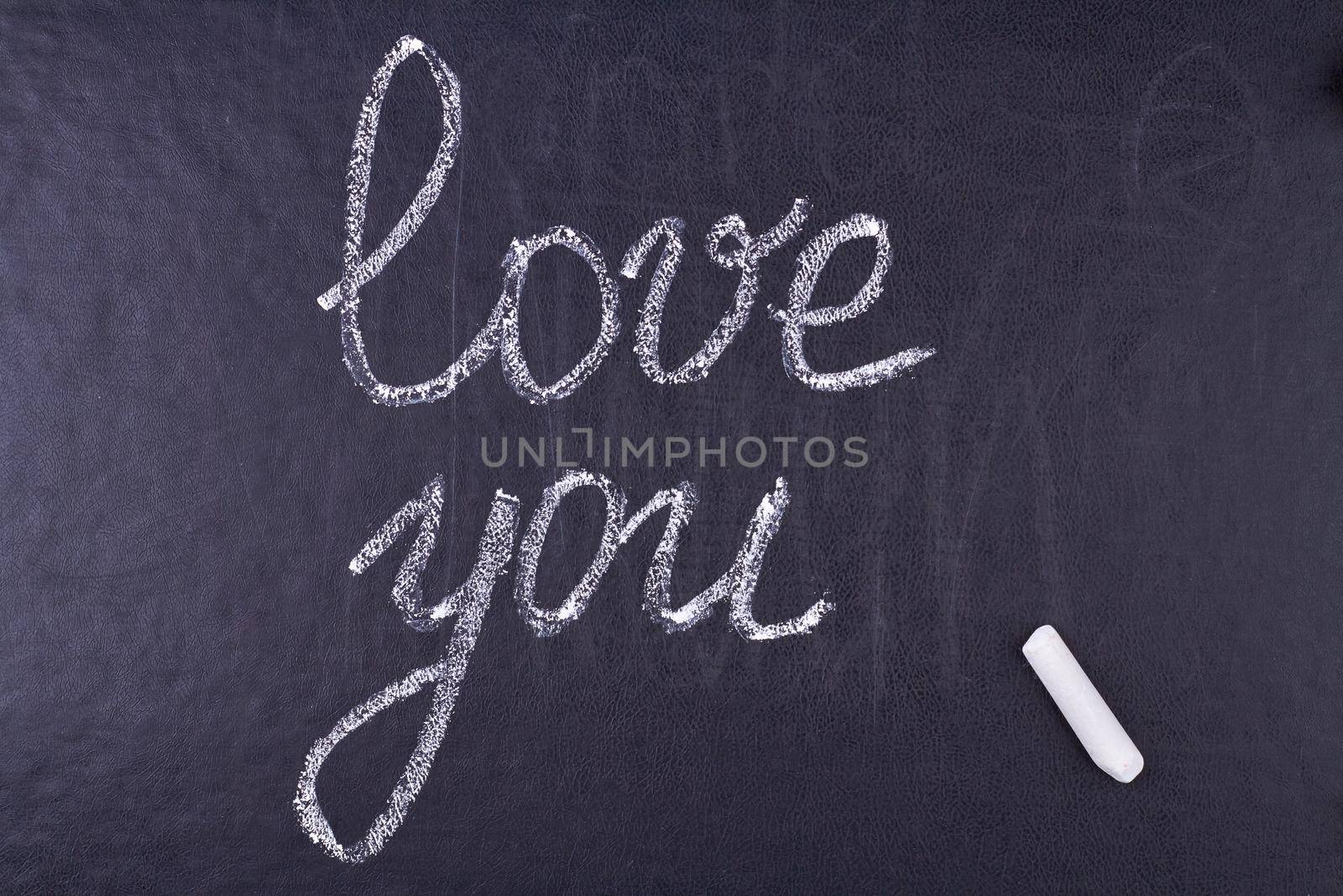 Inscription I Love You and chalk piece on black stone background. Love message.