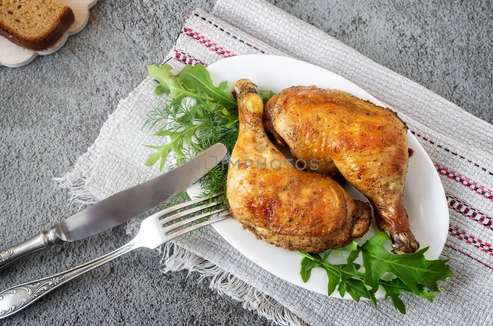 On the table on a linen napkin, a plate with baked chicken drumsticks and greens. Next to bread, spices. The view from the top.