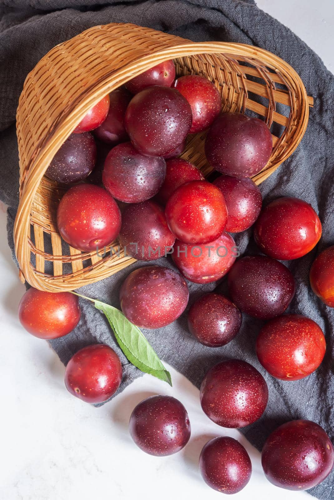 Large ripe plums spilled out of an overturned wicker basket onto a napkin on the table