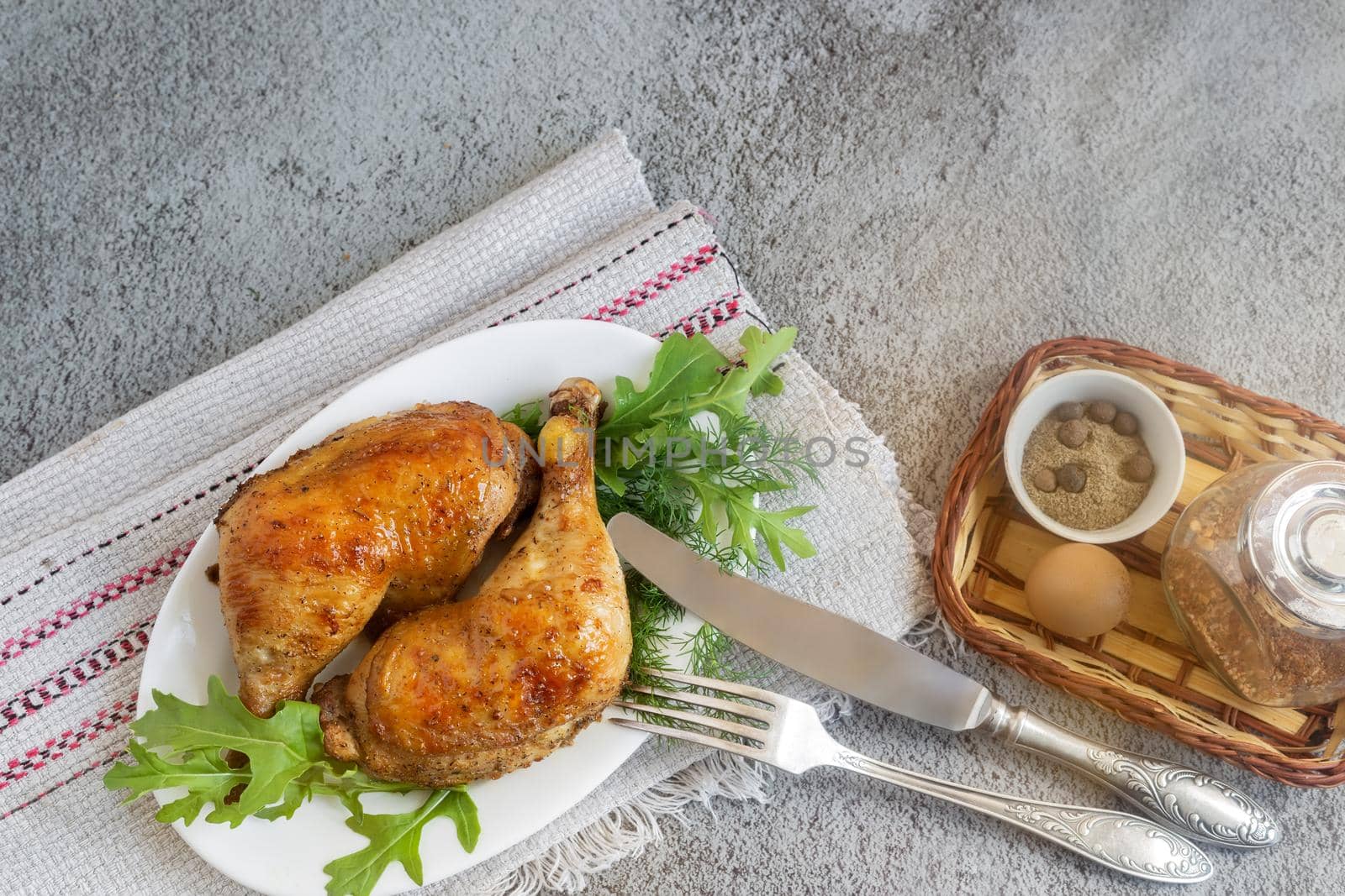 On the table on a linen napkin is a plate with baked chicken legs and herbs. Next to the bread-spices. Top view, copy space