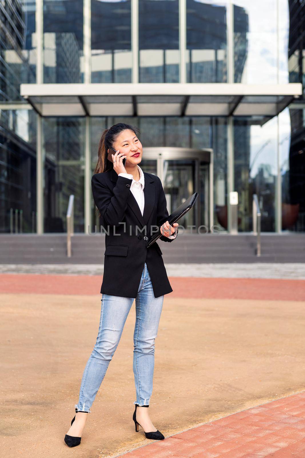 asiatic business woman talking by phone in front of an office building, concept of work and communication, copy space for text