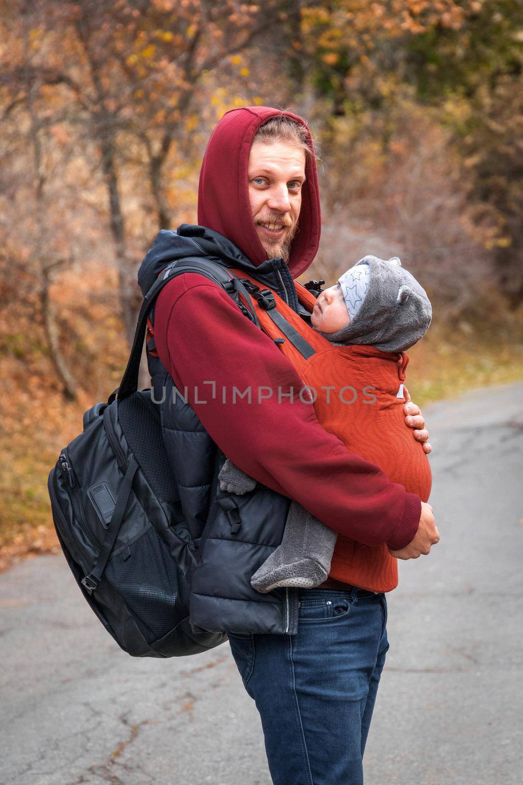 Young bearded babywearing father with his baby in sling autumn walking.