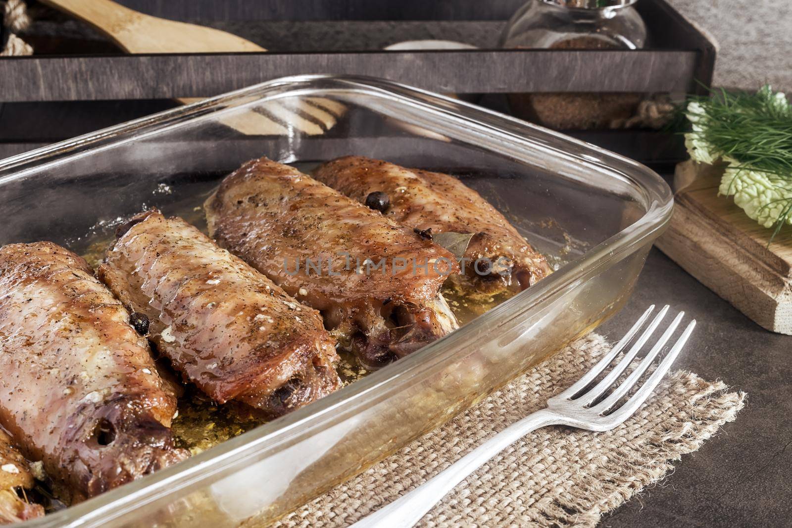 On a wooden table on a napkin is a tray with baked Turkey wings. Next to it are spices and herbs