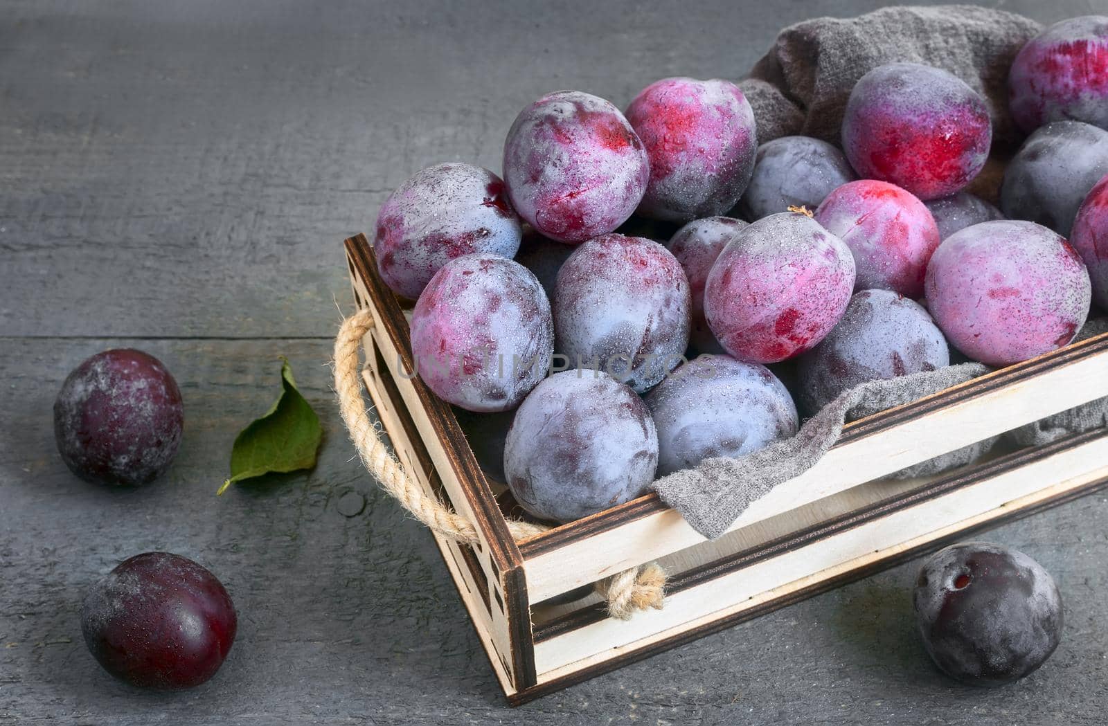 On the table in a drawer are large ripe plums. Presented in close-up on a dark background. The view from the top.