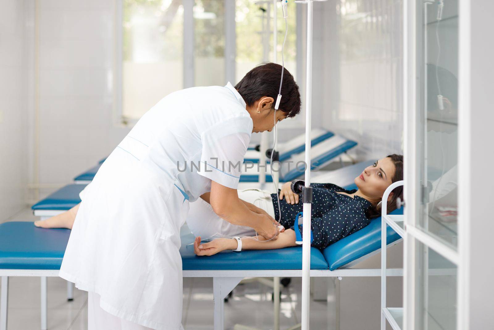 Nurse attaching intravenous tube to patient's hand in Qazaqstan hospital bed.