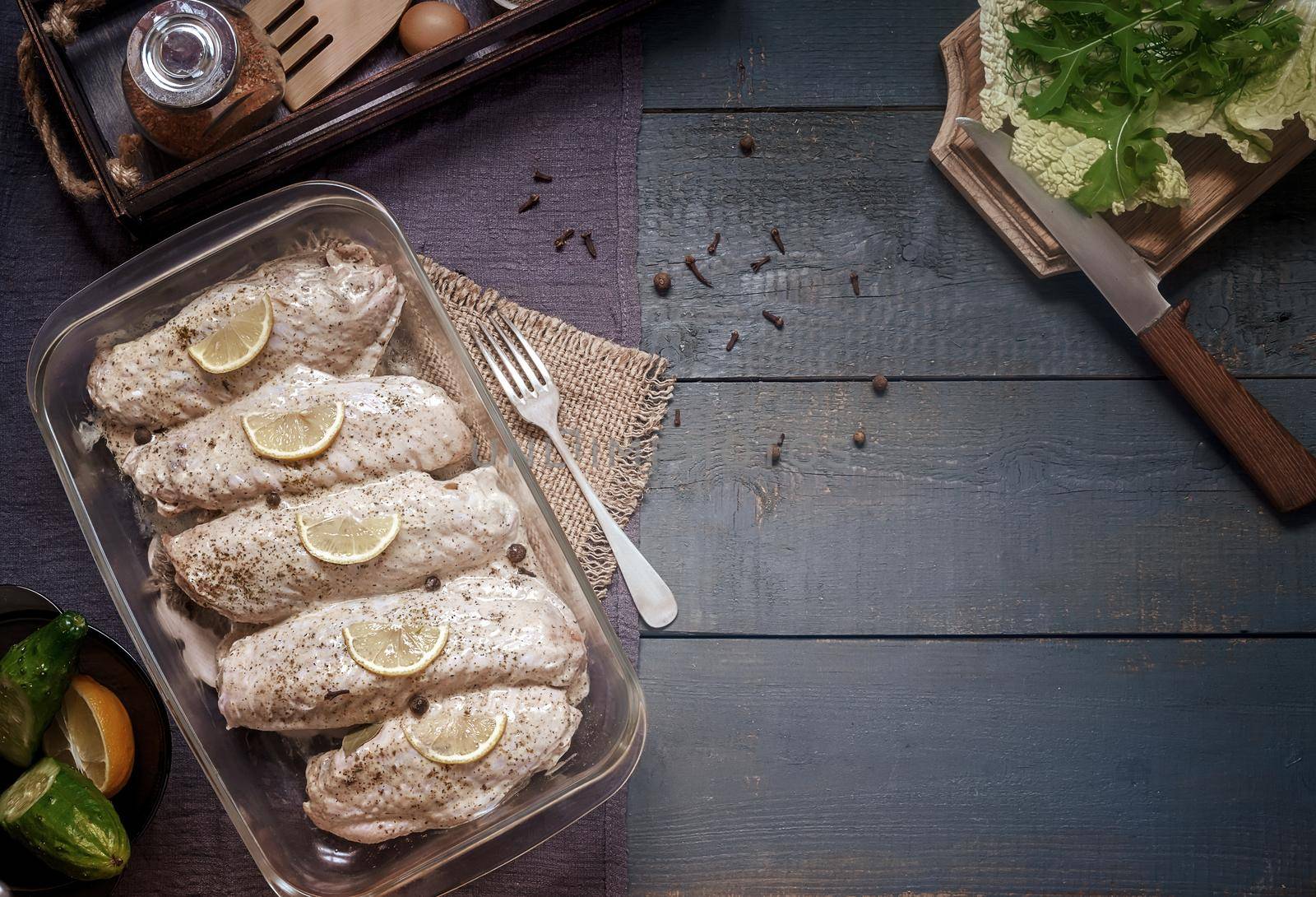 Marinated Turkey wings in a tray on a wooden table, prepared for roasting in the oven. There are spices and herbs nearby. Top view, copy space.