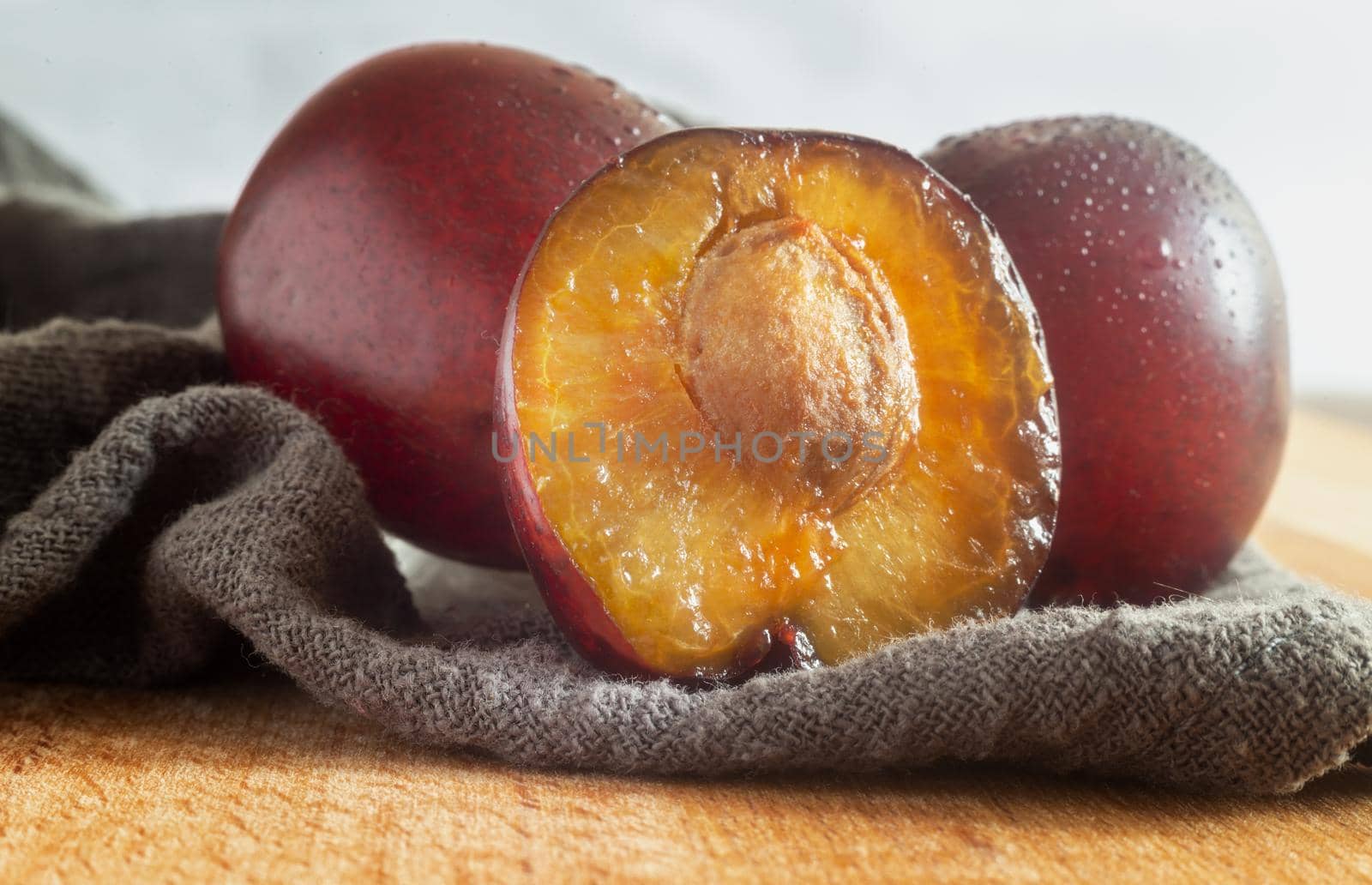 On the wooden table are large ripe plums, one of them is cut off and the stone is visible. Close-up, front view.