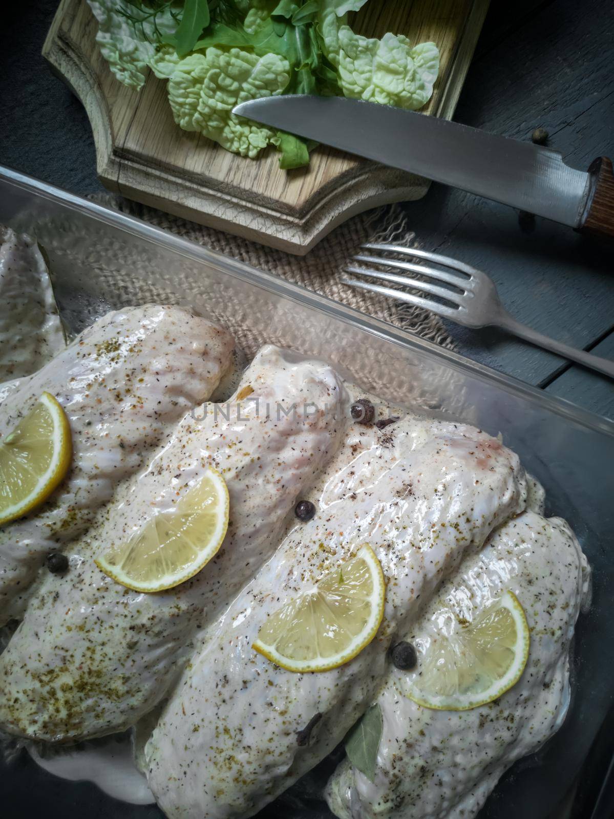 Marinated Turkey wings in a tray on a wooden table, prepared for roasting in the oven. There are spices and herbs nearby.