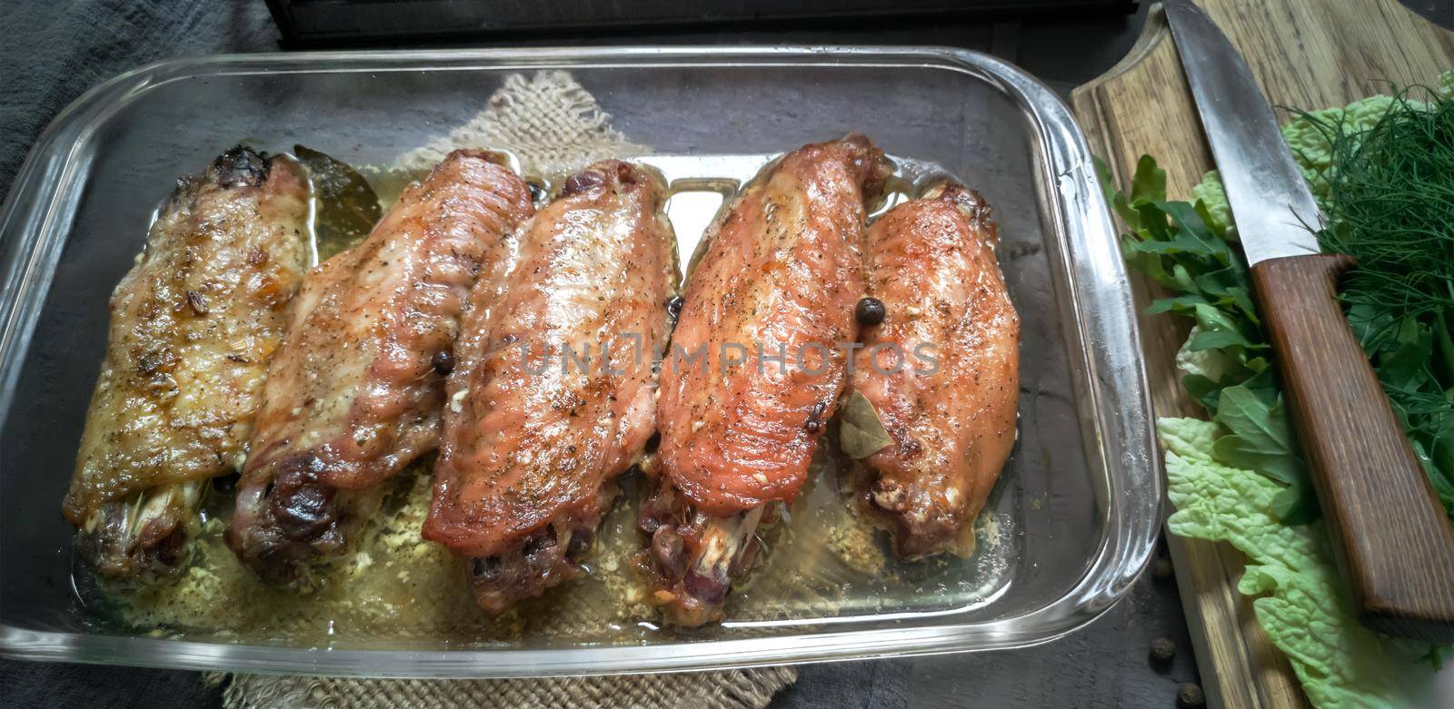 On a wooden table on a napkin is a tray with baked Turkey wings. Next to it are spices and herbs