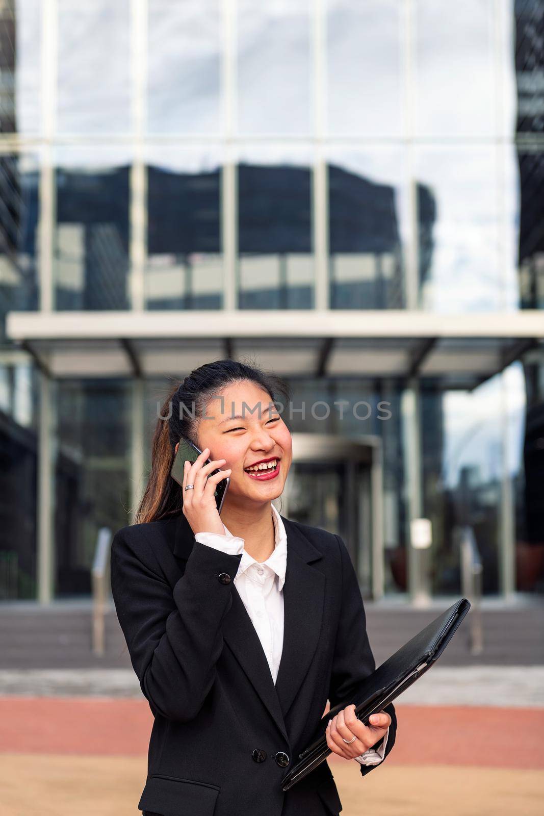 happy asiatic business woman talking by phone in front of an office building, concept of work and communication, copy space for text