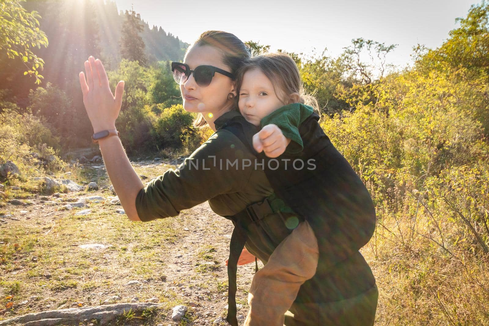 Babywearing mother with her daughter in ergonomic back sling in sunny day of summer outdoor.