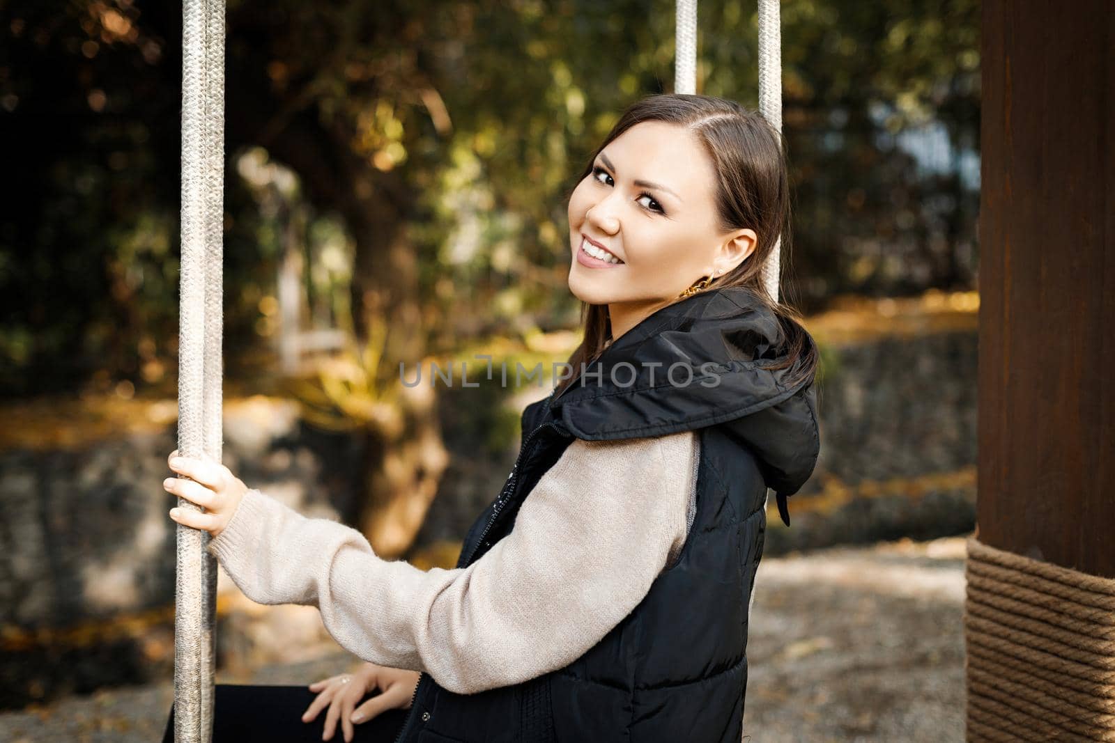 Beautiful young smiling woman sitting on a swing in autumn in a park outdoors. High quality photo