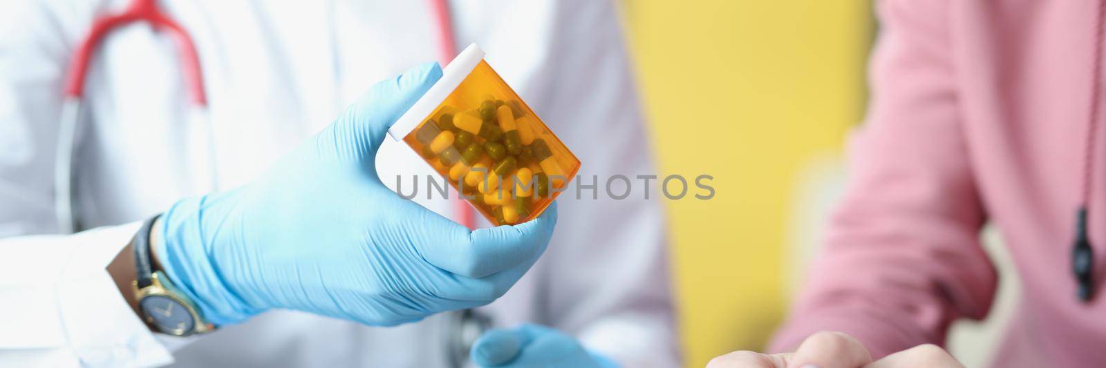 Close-up of therapist hand holding bottle with capsules. Female patient at doctor appointment. Blisters of pills on table. Medical prescription, treatment and healthcare concept