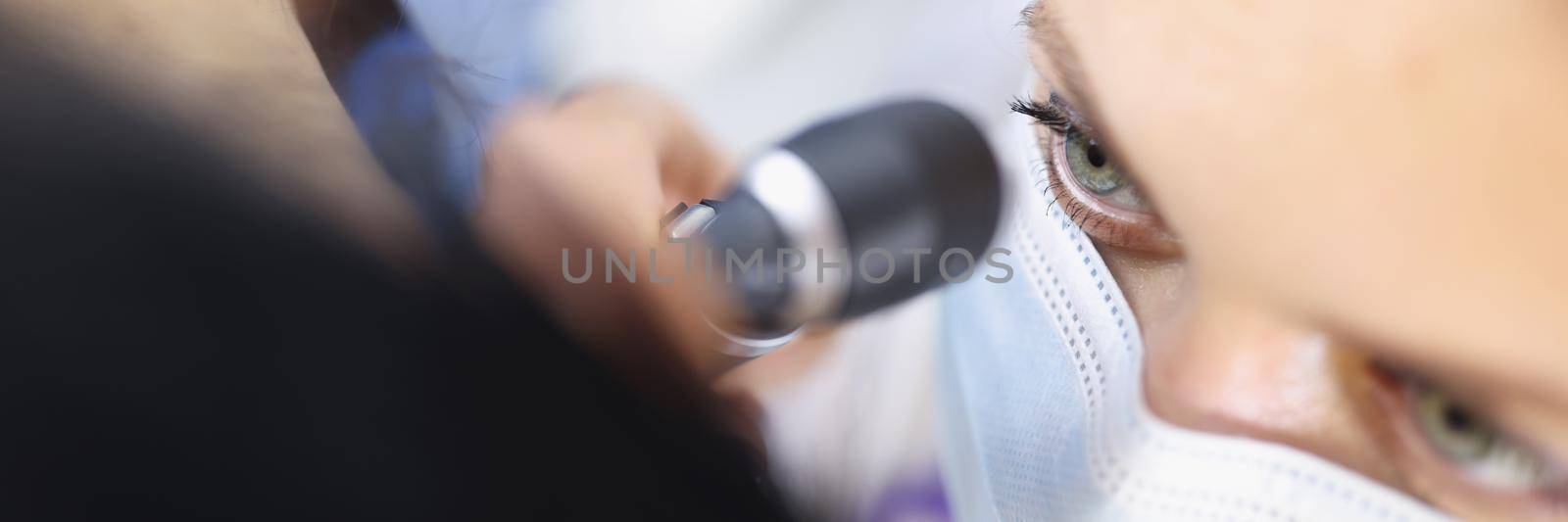 Top view of female ent doctor in medical mask examining ear with otoscope carefully. Patient at practitioner appointment. Otolaryngology, medicine and healthcare concept