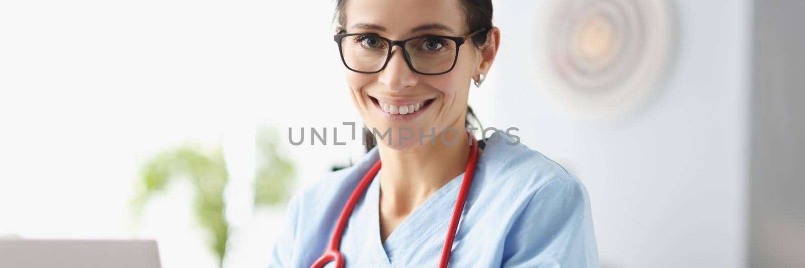 Portrait of woman therapist posing in clinic office. Smiling woman physician sitting at table in consulting room. Cheerful practitioner working with documents. Medicine and healthcare concept