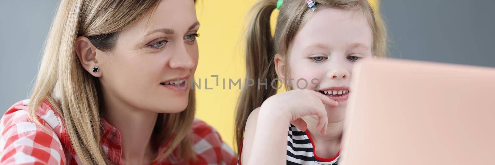 Portrait of mother and daughter spend time together watching cartoons, quality time with parent and child, laptop on table. Family, leisure, education, fun, parenthood, childhood concept