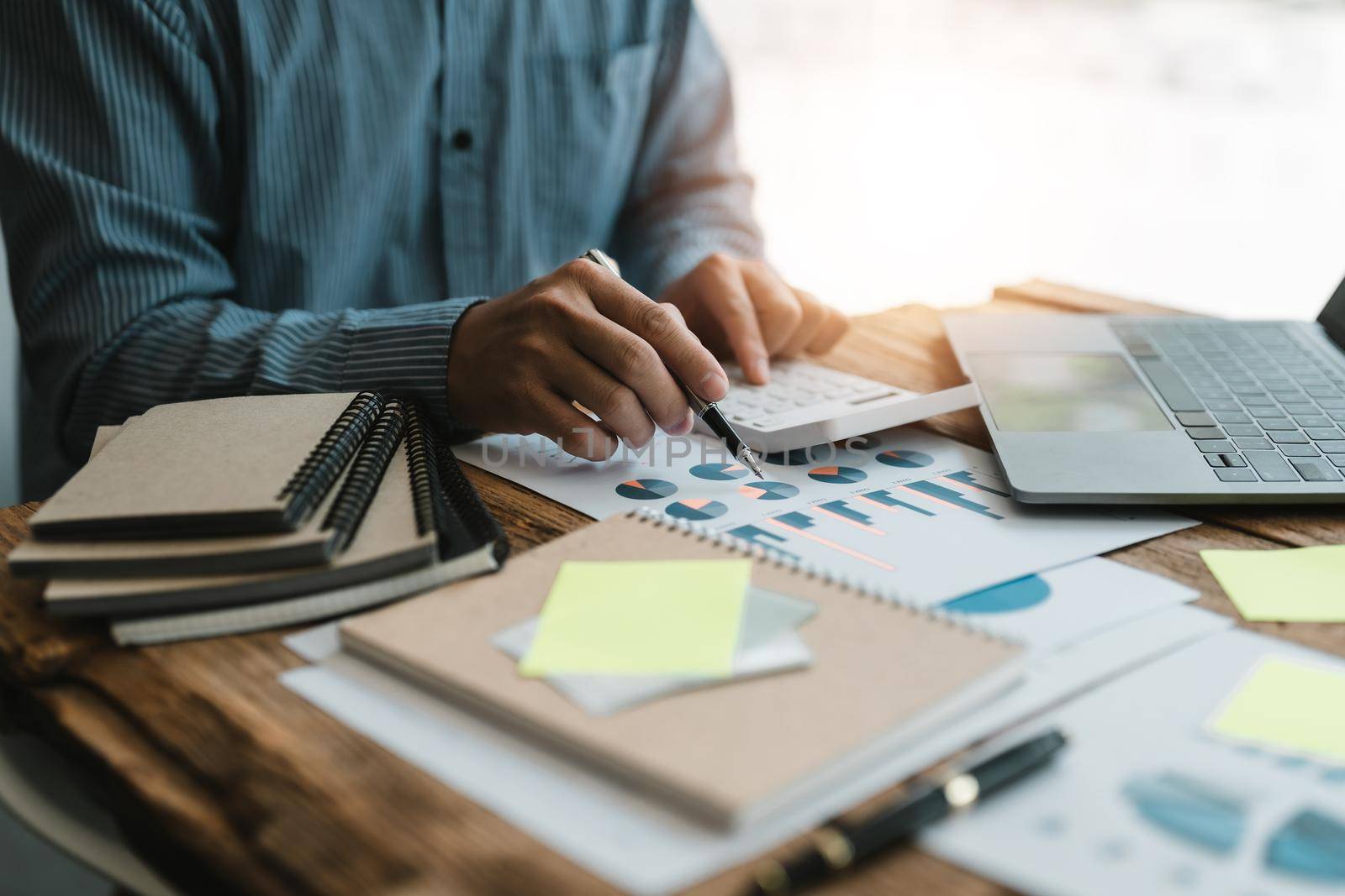 Close up of businessman or accountant hand holding pen working on calculator to calculate business data, accountancy document and laptop computer at office, business concept.
