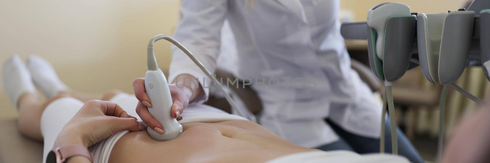 Close-up of gynecologist doing ultrasound scan in modern clinic, doctor in white lab coat examining woman. Female patient expecting pregnancy. Medicine, gynecology, health concept