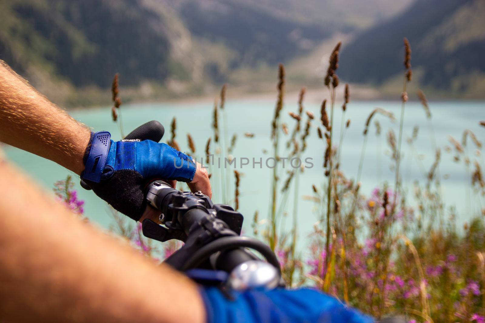 Close-up of hands in sports gloves on the handlebars of a mountain bike against the backdrop of a mountain lake.