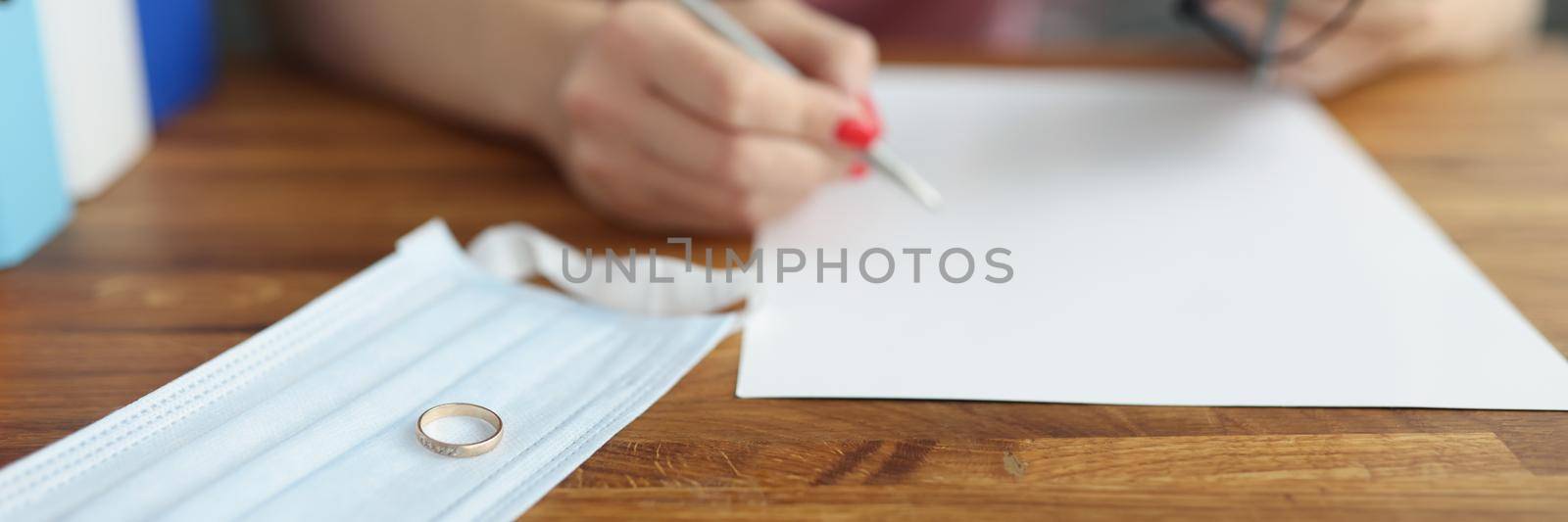 Close-up of ring on protective face mask, female signing decree of divorce. Filing divorce papers or premarital agreement prepared by lawyer. Canceling marriage, legal separation documents concept