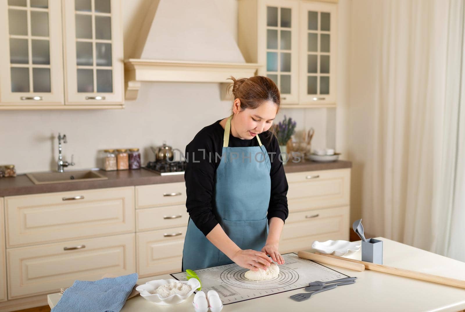 Young Central Asian woman cooking from dough in modern kitchen.