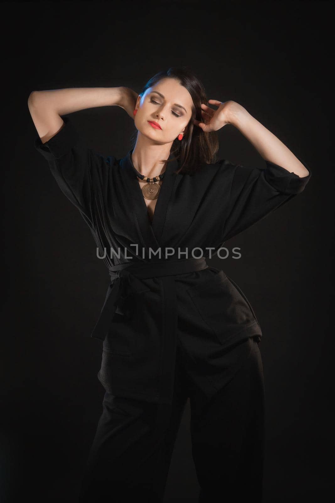 Studio shot in low key with woman with raised hands in black clothes.