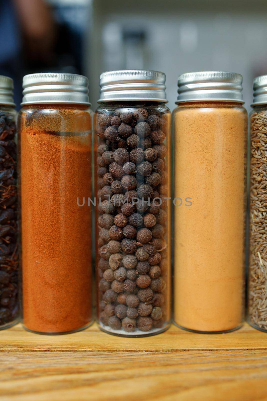 Paprika, sweet peas and ginger in transparent jars among other spices on the table in home kitchen.