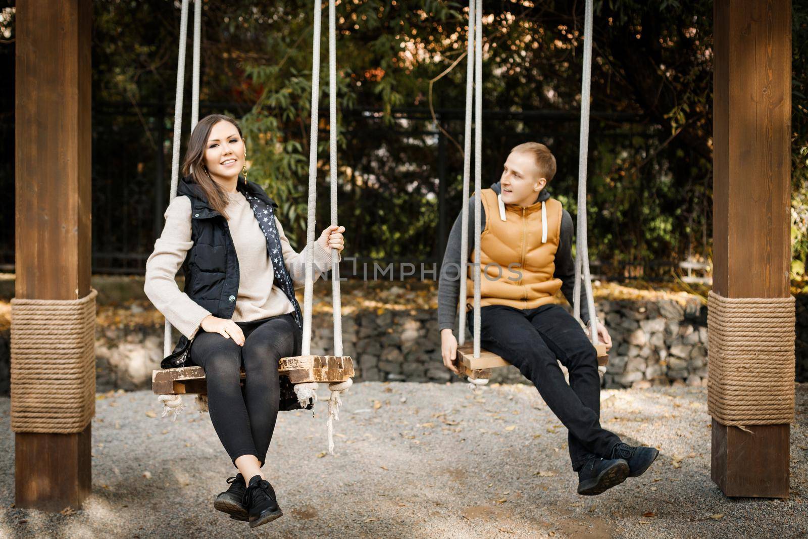 A young man with his lover are sitting on a swing in the forest among the trees. High quality photo
