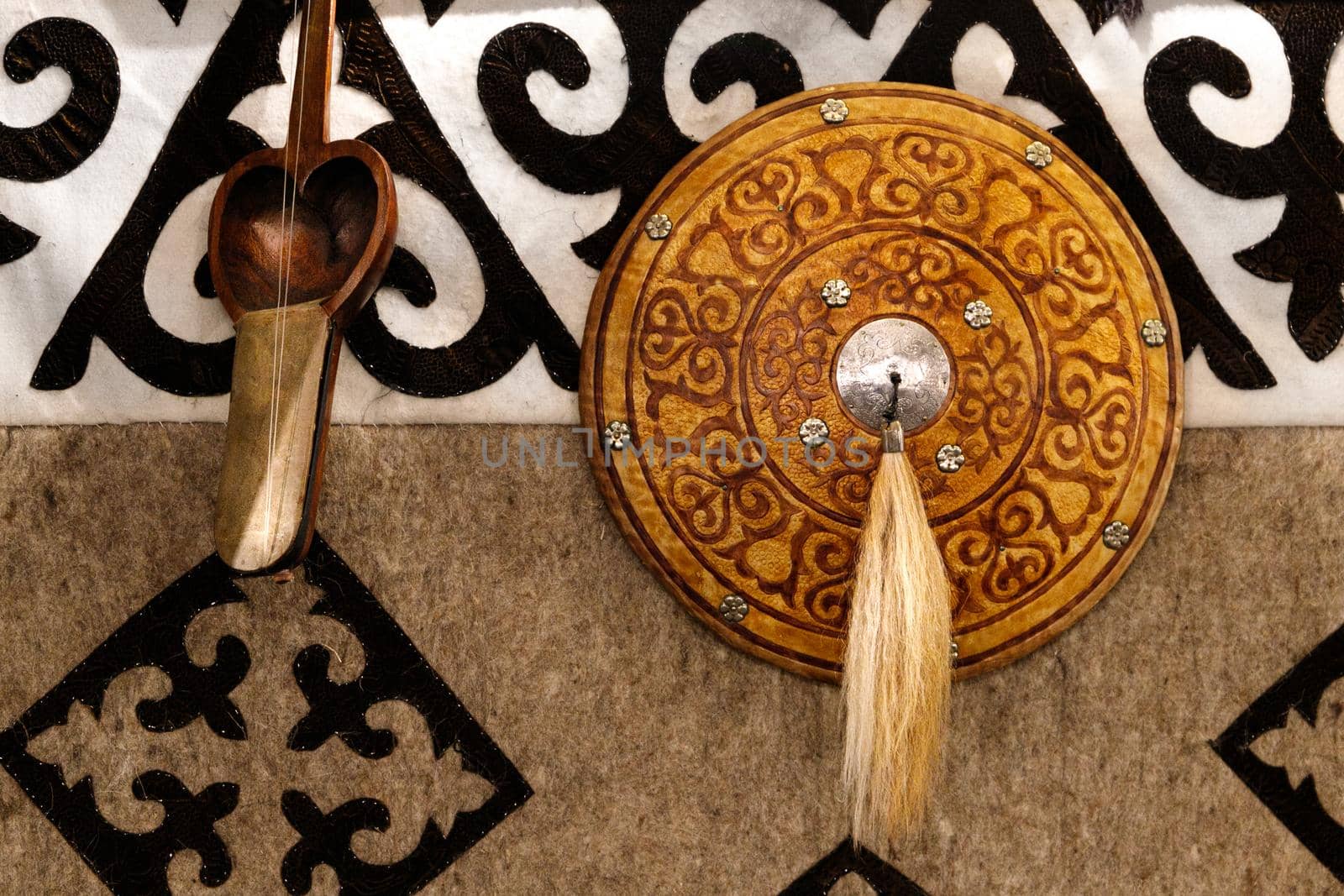 Kazakh musical instruments and decorative shield on the background of a felt carpet with national patterns.