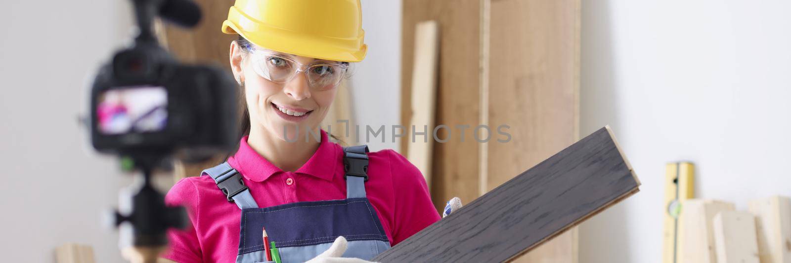 Portrait of professional female worker holding laminate board and showing to camera. Repairer perform construction task, renovation in home. Building blogging and vlogging idea. Redecoration concept