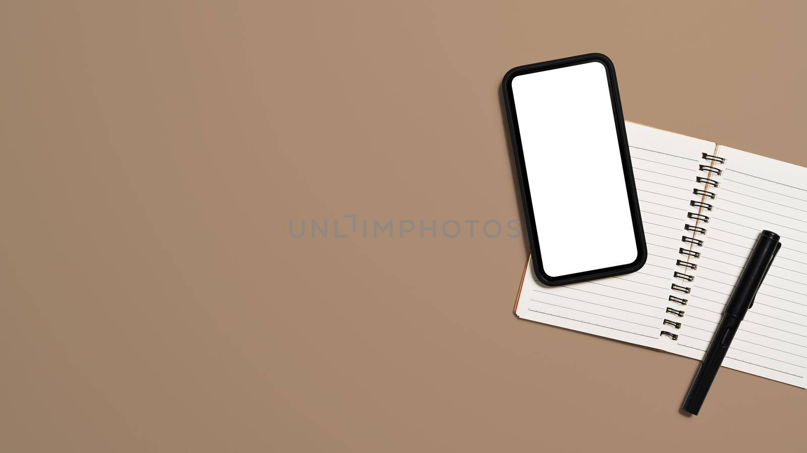 Top view mobile phone with empty screen ad notebook on beige background. Copy space by prathanchorruangsak