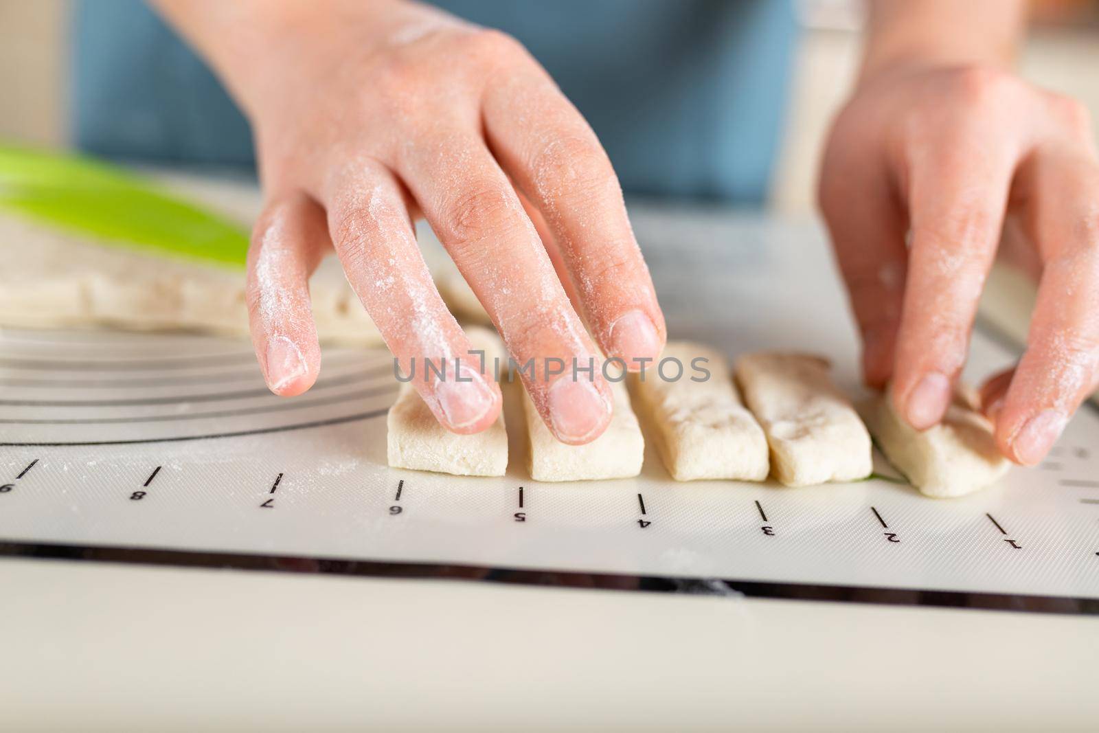 Close-up of floured hands spreading pieces of dough along the markings on a silicone baking mat.