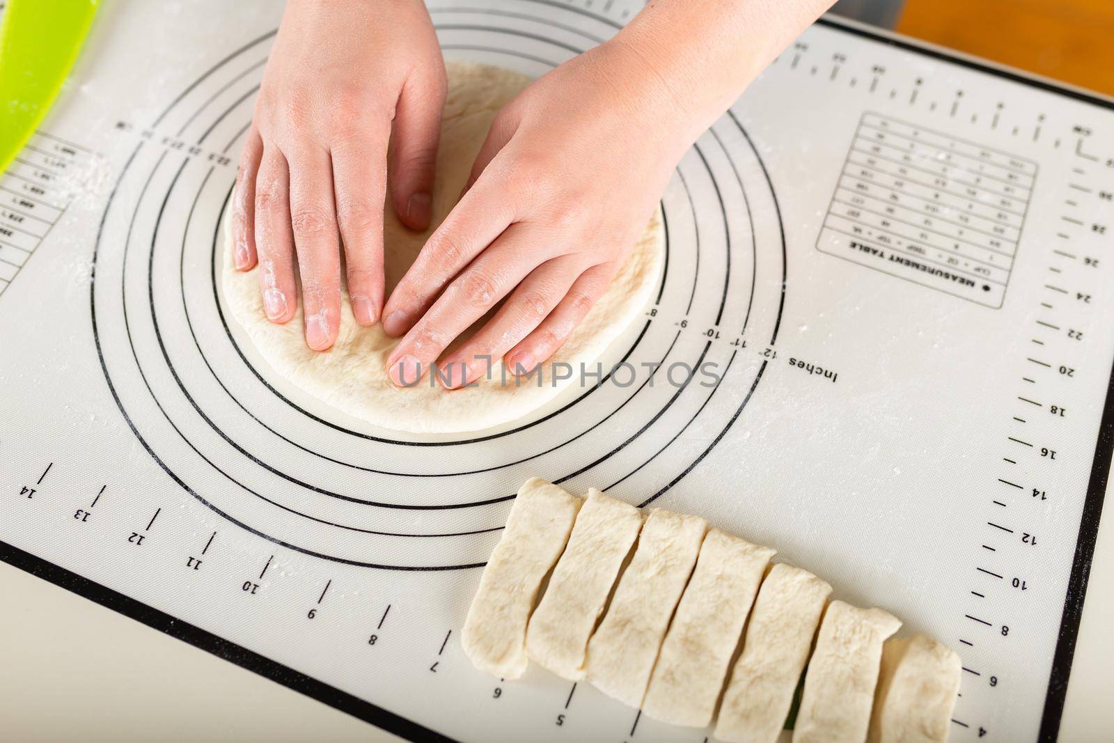 Close-up of hands kneading rolled out dough on a kitchen silicone mat with round markings of different diameters.