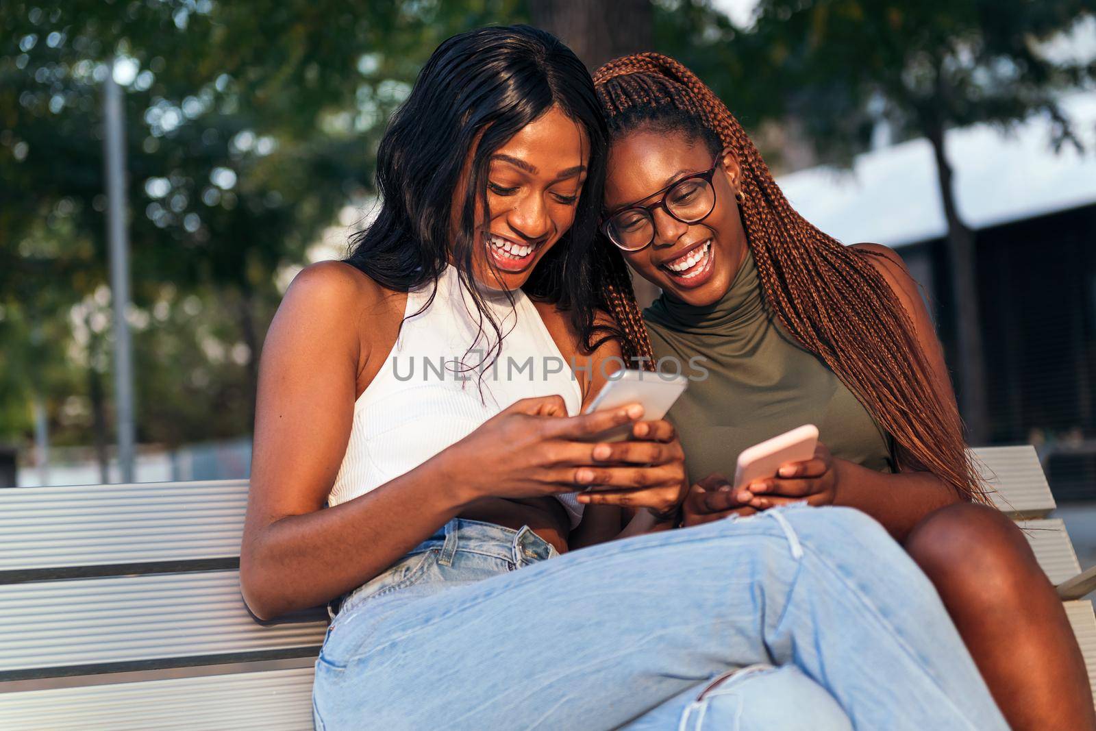 two young black women laugh out loud looking at their social networks on their mobile phones, concept of youth and fun, copy space for text