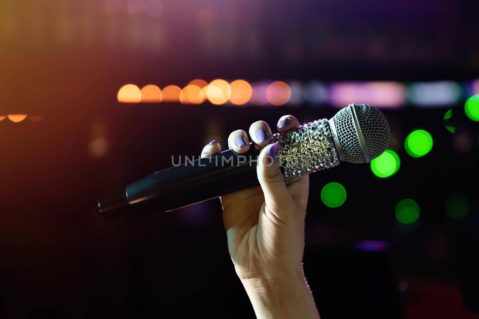 Woman hand holding wireless microphone with rhinestones on stage.