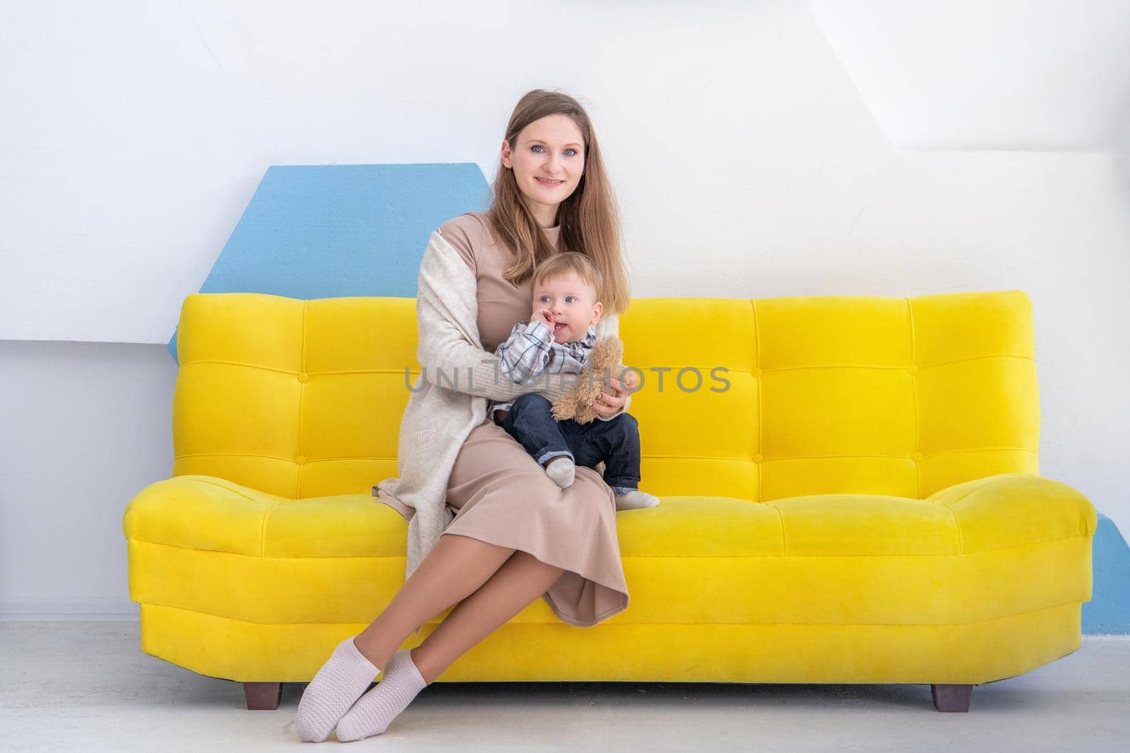 Portrait of a young european woman with a small child on a sofa in a bright positive interior.