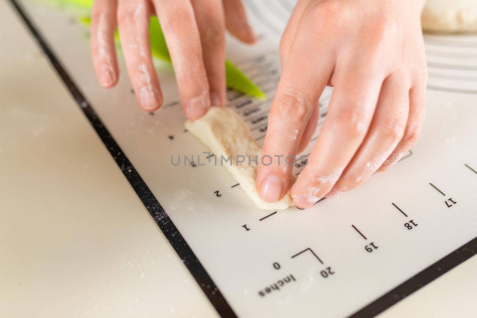 Close-up of hands measuring the length of a piece of dough on a kitchen mat with inch markings.